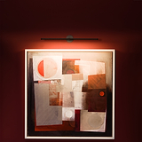Peinture abstraite aux formes géométriques éclairée par une Taylor Picture Light sur fond rouge.