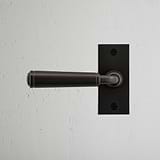 Poignée de Porte à Plaque Courte Digby de couleur bronze contre un mur texturé blanc, rehaussant l'élégance de la porte.