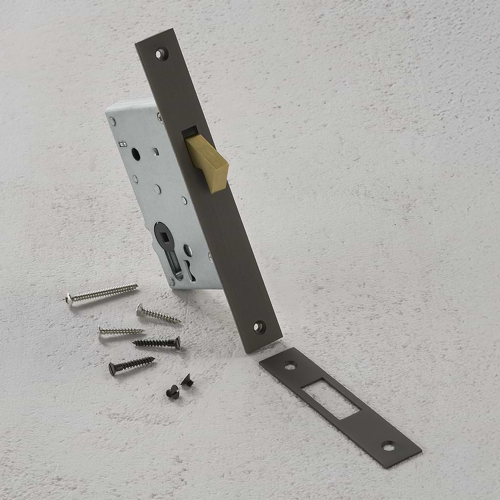 Fechadura de gancho 60 mm em bronze montada com parafusos sobre superfície texturizada branca.
