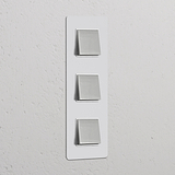 Interruptor triplo vertical de três vias em Níquel Polido Pintável Branco montado em parede texturizada branca.