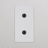 Interruptor duplo vertical com dois botões, acabamento bronze pintável, para uso bidirecional.