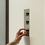 Ajustando manualmente o 'Interruptor regulador vertical de três vias triplo – Níquel Polido' em painel de parede.