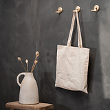 Gancho Portland – Latão Antigo segurando uma bolsa bege ao lado de um vaso com flores secas.