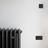 Bronze 1G two way toggle switch on white wall with black radiator and bronze double socket below