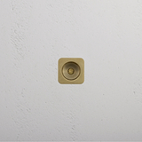 A gold square light switch on a white textured wall exudes elegance, like antique brass.