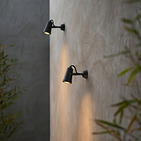 Pair of bronze Cambridge Wall Spotlight 24V outdoor spotlights mounted on a beige wall, plants in foreground.