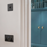 Bronze and black double socket with USB fixed to cream wall with bronze toggle switch above and sea blue cupboard with antique brass cupboard handles to the right