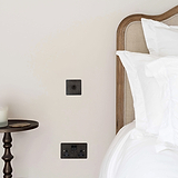 Bronze 1G two way toggle switch on white wall next to wooden framed headboard and white bedding