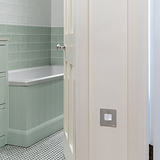 Polished Nickel and white switched fused spur fixed to cream wall outside pastel green bathroom 