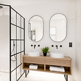 Bronze and black shaver socket fixed to white wooden slatted bathroom wall above woodenbasin pedestal next to bronzze taps and a bronze framed mirror