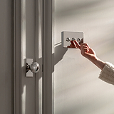 Polished nickel 3G two way toggle switch fixed to cream wall with person setting switch to on position next to cream door with polished nickel Poplar door handle 
