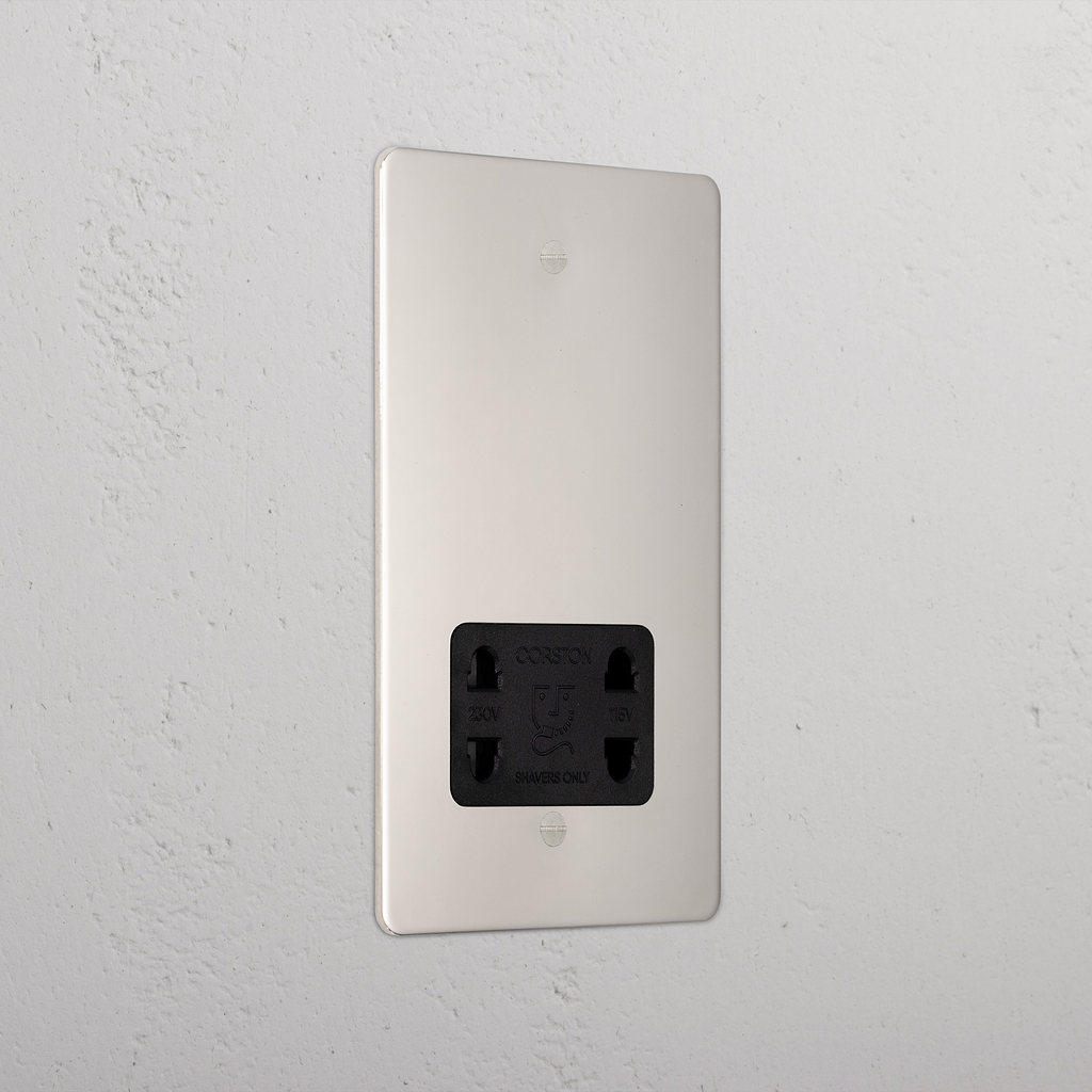 Polished nickel shaver socket with black insert on grey wall. 