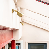 Antique Brass Bayliss Single 50mm Spotlight fitted  to a white wall on the left with red metal beam beneath. 