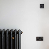 Bronze 1G two way toggle switch on white wall with black radiator and bronze double socket below