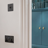 Bronze and black double socket with USB fixed to cream wall with bronze toggle switch above and sea blue cupboard with antique brass cupboard handles to the right 