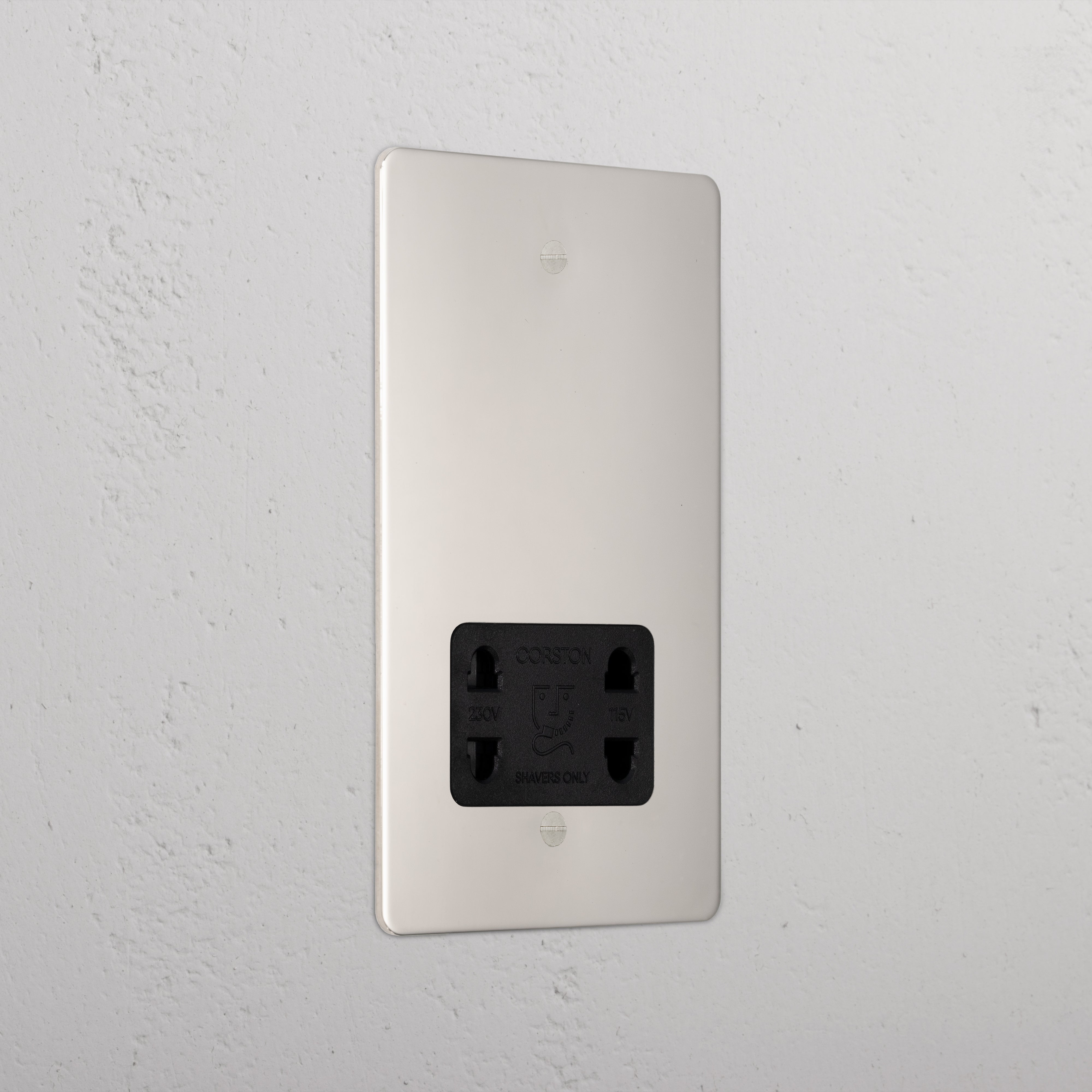 Polished nickel shaver socket with black insert on grey wall. 