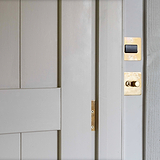 Antique brass and black fan isolator switch fixed to cream wall above dimmer and toggle switch and next to cream slatted wooden door 