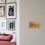 Antique Brass 3G two way dimmer switch on whitewall with framed pictures and a dusky pink settee in the background