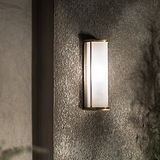 Medium wall light featuring fluted glass and antique brass finish, mounted on a gray wall, softly illuminated.