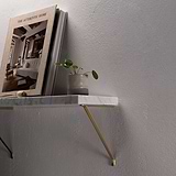 Antique Brass Brixton Shelf Bracket 200mm supporting a white marble shelf on a textured white wall holding a book and a mini plant in plant pot. 