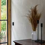 Bronze Dimmer Switch On Cream Wall With Candlesticks And Dried Flowers On Wooden Table