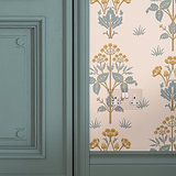 Clear white double socket painted pastel green fixed to wall with pastel green and orange floral wallpaper next to pastel green wooden door