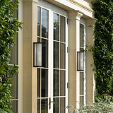 Medium wall light in bronze finish with fluted glass shade, mounted on a light stone wall by French doors.