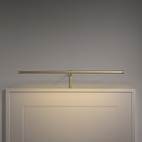 Antique brass minimalist Harrow Picture Light 580mm, mounted above a framed panel on gray wall.