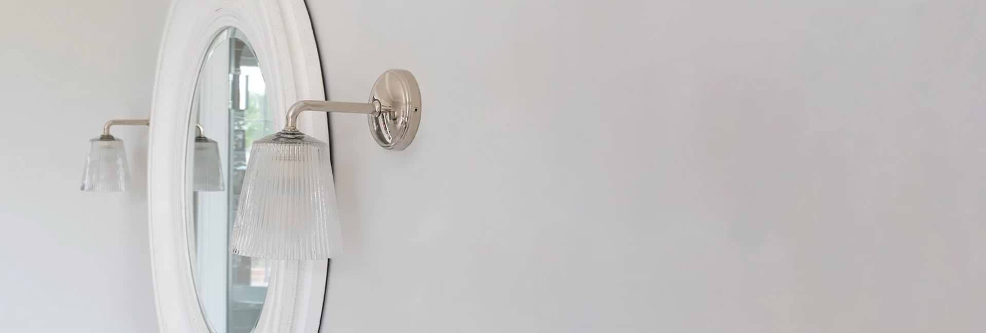 Zwei Wandleuchten Poliertes Nickel an einer weißen Wand links und rechts von einem Badezimmerspiegel