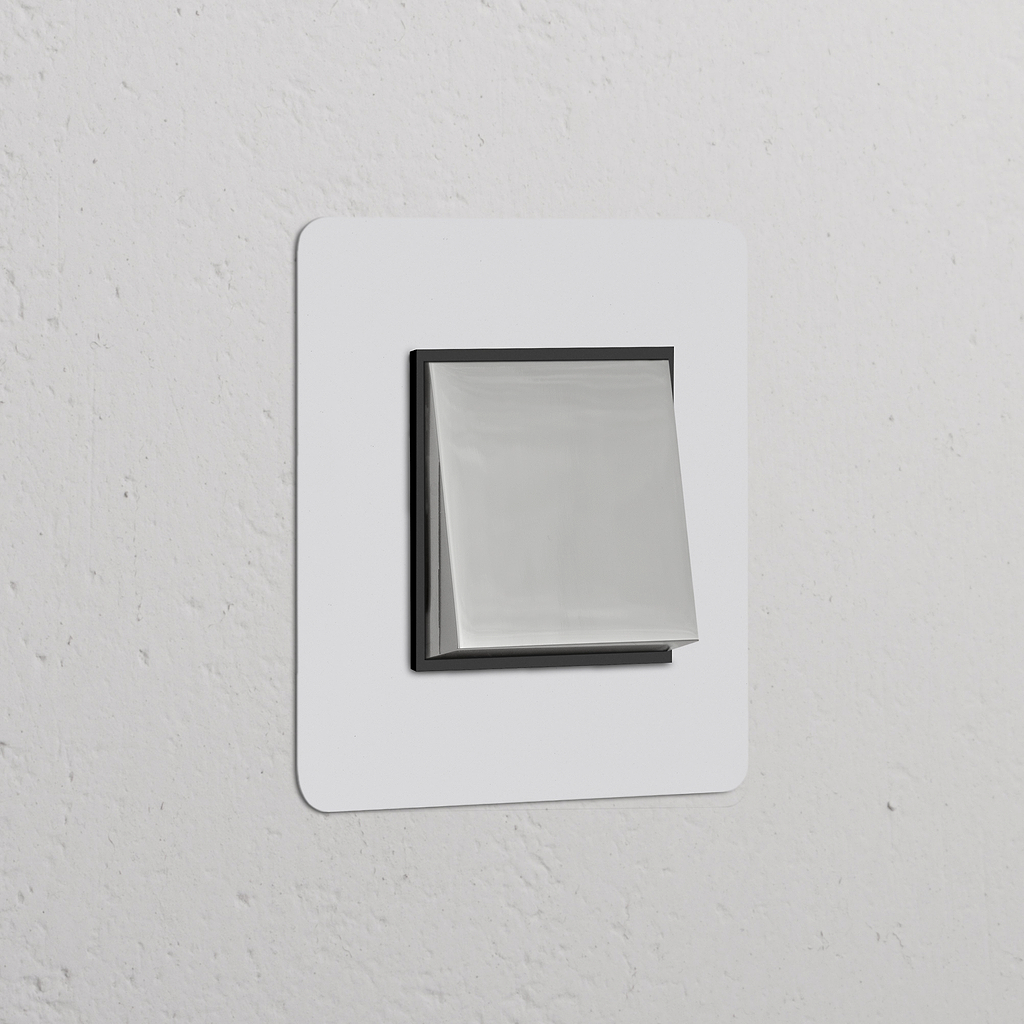Moderner Einfachrahmen mit Wippschalter, lackierbar, poliertes Nickel und Schwarz, auf weißer Wand.