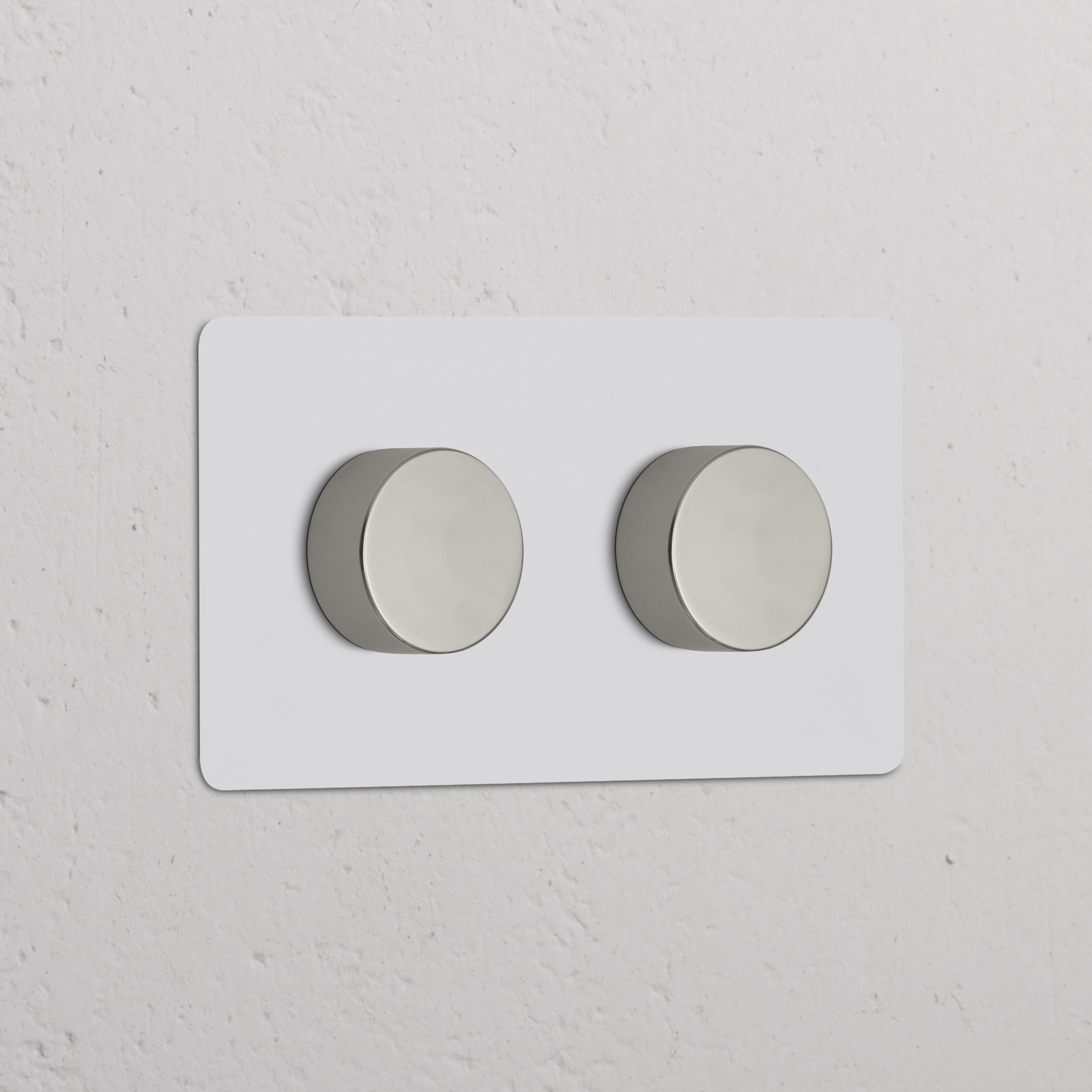 Zweifachrahmen mit 2x Mehrpunkt-Dimmerschalter, lackierbar und poliertes Nickel, an weißer Wand montiert.