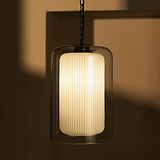 Pendelleuchte mit geripptem Glasschirm namens „Nan“, die ein warmes Licht verbreitet.