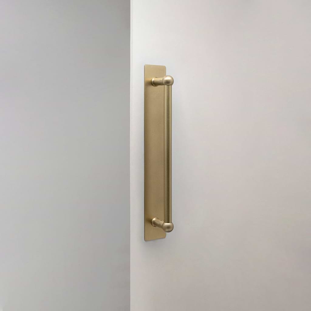 Antieke Harper-deurkruk van messing met plaat van 320 mm op een witte deur, bekeken vanaf de zijkant.