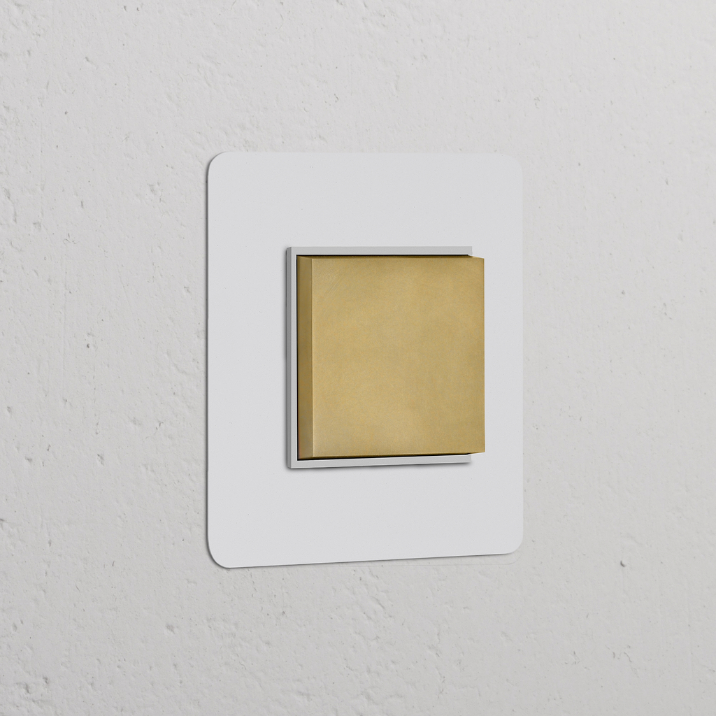 Wandschalter mit zentrierter Wippe in einem einfachen Rahmen, lackierbares Finish in Antikmessing und Weiß, auf einer strukturierten Wand.