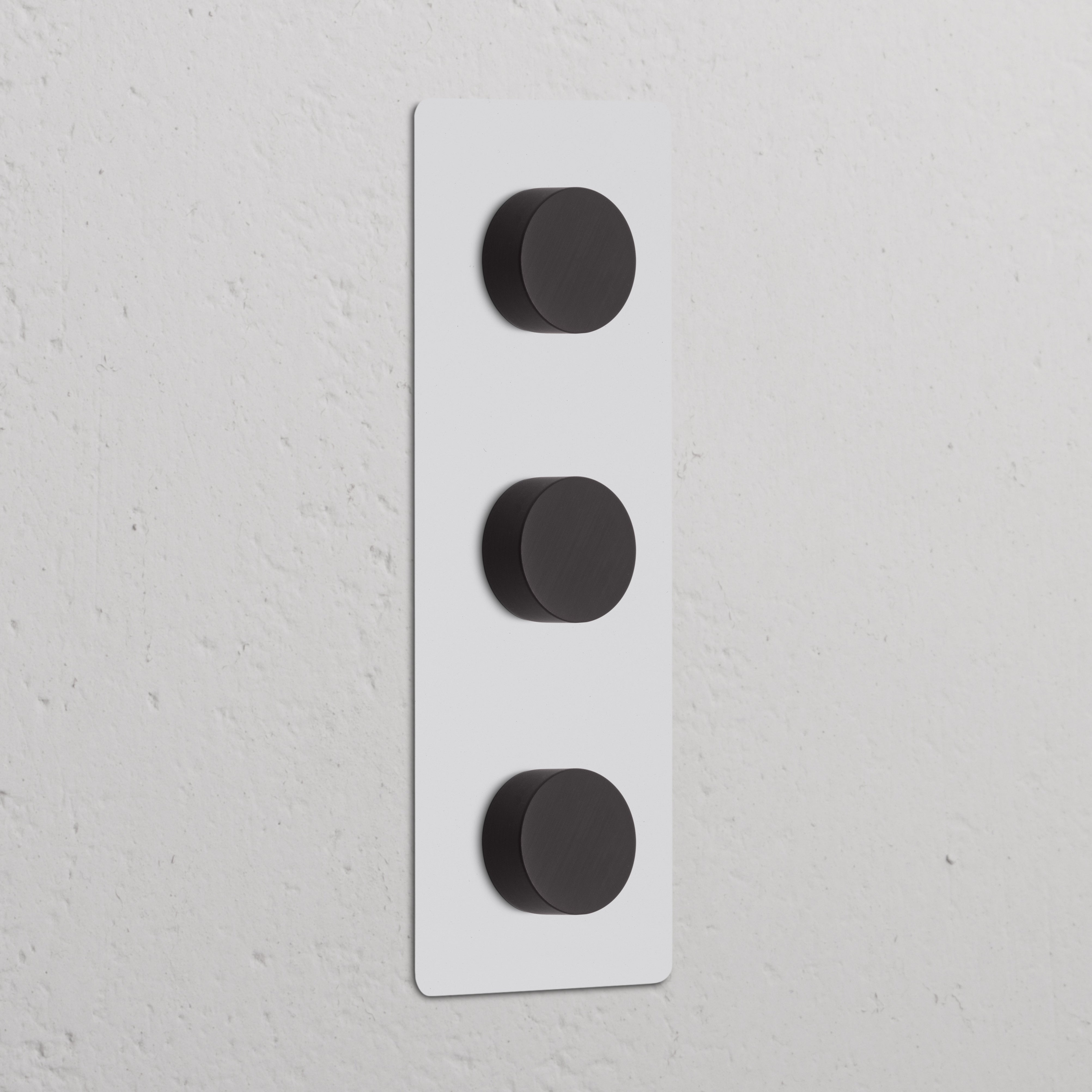 Vertikaler Dreifachrahmen mit 3x Mehrpunkt-Dimmerschalter, lackierbar und Bronze, montiert an weißer Wand.