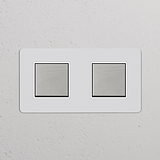 Zweifachrahmen mit 2x Wippschalter – lackierbar, poliertes Nickel, weiß – auf einer weißen Wand montiert.