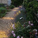 Ealing Wegestrahler – Außenbeleuchtung aus poliertem Nickel zur Beleuchtung eines Gartenwegs mit Blumen und Büschen.