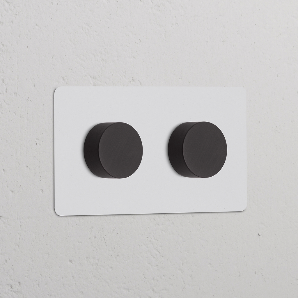 Zweifachrahmen mit 2 Dimmerschaltern, lackierbar und bronzefarbenes Finish, schlankes Design auf einer strukturierten Wand.