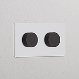 Zweifachrahmen mit 2 Dimmerschaltern, lackierbar und bronzefarbenes Finish, schlankes Design auf einer strukturierten Wand.