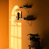 Bronzene Brixton-Regalhalterung (200 mm) an einer orangefarbenen Wand, trägt Regale mit Dekor und Büchern.