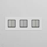 Dreifachrahmen mit 6x Wippschalter – Lackierbar, Poliertes Nickel und Schwarz, vor einer weißen Wand.