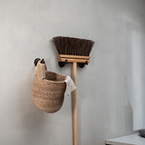 Hyde Haken – Bronzener Kleiderbügel an einer minimalistischen Wand, gepaart mit einem Besen.