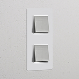 Vertikaler Zweifachrahmen mit 2x Wippschalter, lackierbar, in poliertem Nickel auf weißer Wand.