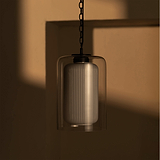 Hängende Pendelleuchte mit geriffeltem Glasschirm, der stimmungsvolles Licht an einer beigen Wand erzeugt.