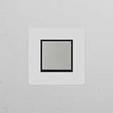 Zwischenschalter im Einfachrahmen mit Wippschalter, lackierbar, poliertes Nickel und Schwarz, auf weißer Wand.