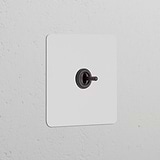 Aufputz-Tastschalter mit zentriertem Kipphebel in lackierbarer Ausführung oder Bronze, Einfachrahmen-Design.