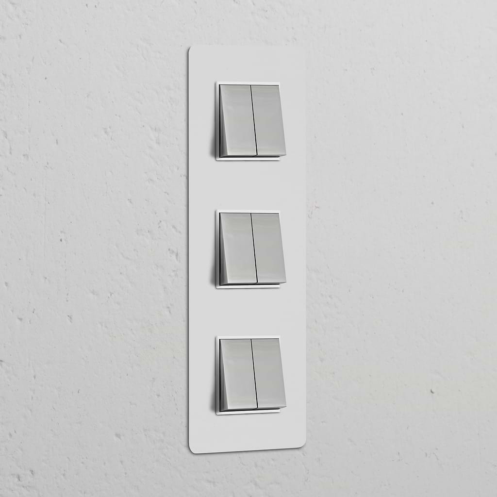 Vertikaler Dreifachrahmen mit 6 Wippschaltern, lackierbar, poliertes Nickel und Weiß auf weißer Wand.