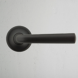 Ungefederter Türgriff von Apsley in Bronze-Finish, elegantes Design für Türen vor einer weißen strukturierten Wand.