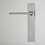 Clayton gefederter Türgriff langes Schild – Poliertes Nickel Türgriff auf rechteckigem Schild vor weißer Wand.