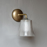 Richmond Medium-Wandleuchte mit geriffeltem Glas und antikem Messing an einer grauen, strukturierten Wand montiert.